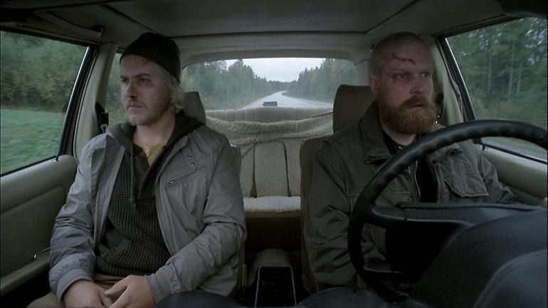 Bild ur filmen Höstmannen. Två män sitter i framsätena på en bil, de ser sårade och omtumlade ut.