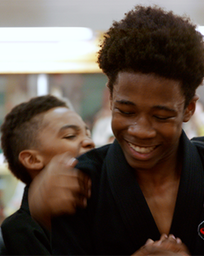 Två killar står i svarta karatekläder och ser glada ut.