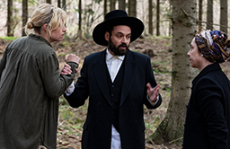 En man i judekläder står och pratar med en man och en kvinna i skogen