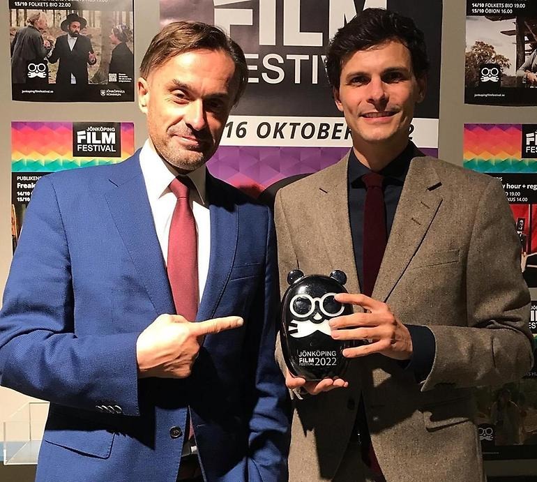 Två män i kostym varav den ena håller i en svart glasutter